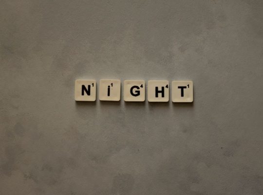 Scrabble tiles arranged to spell 'Night' on a minimalist gray background.
