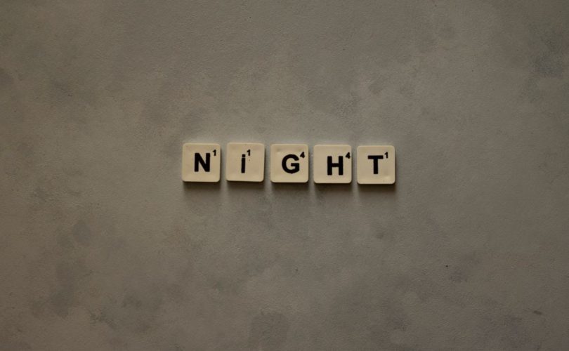 Scrabble tiles arranged to spell 'Night' on a minimalist gray background.